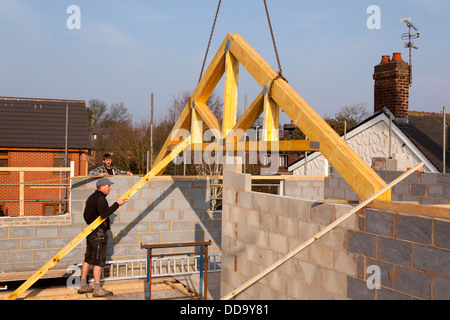 self building house, constructing roof, lifting first trusses with crane, quadruple truss being positioned Stock Photo