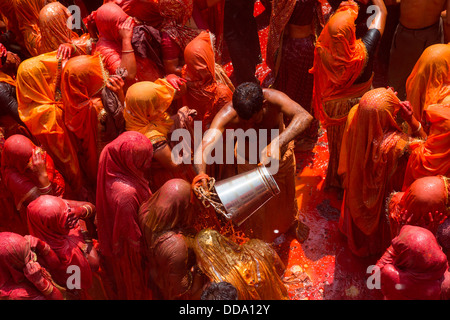 A man throws a pail of water to women in a symbolic battle during the celebration of Holi in Baldeo Stock Photo