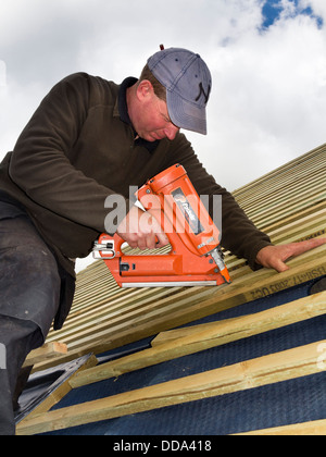 self building house, constructing roof, worker fixing wooden battens using paslode nail gun Stock Photo