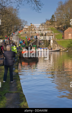 People on busy sunny canal towpath by boats, walking & looking at renovation work - open day, Bingley's Five Rise Locks, West Yorkshire, England, UK. Stock Photo