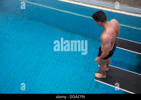 Man standing on diving board at public swimming pool above the water Stock Photo