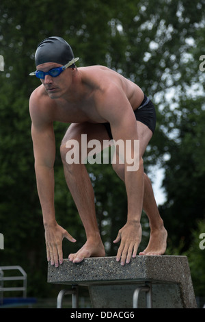 Man standing on starting block at public swimming pool ready to jump Stock Photo