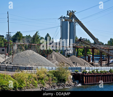 This is an industrial image of a gravel pit with a large silo and belts, along with large piles of various grades of gravel. Stock Photo