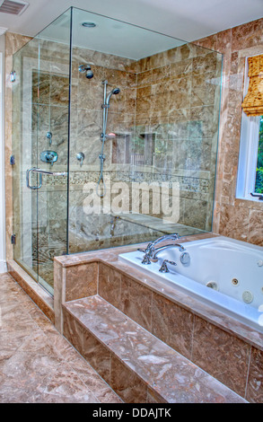 This modern bathroom features a clear glass shower with marble enclosure, and a pretty white bathtub. Stock Photo