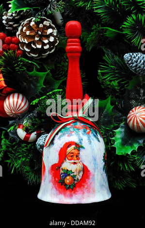 Ceramic Christmas hand bell with wooden handle and Christmas wreath on a black background. Stock Photo