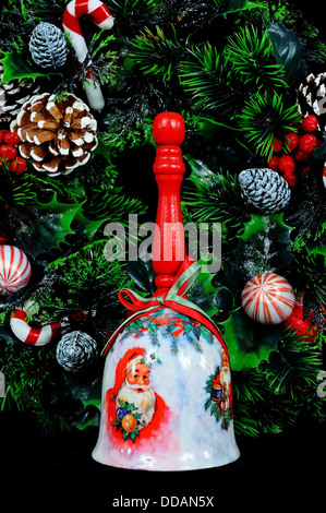 Ceramic Christmas hand bell with wooden handle and Christmas wreath on a black background. Stock Photo