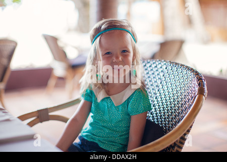 Little girl sitting in chair at restaurant waiting for her food Stock Photo