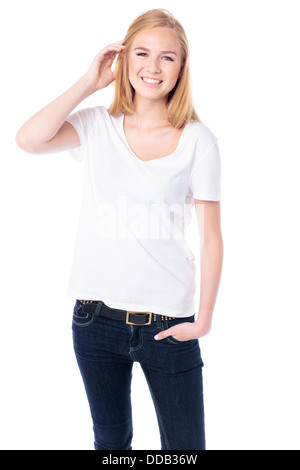 Happy young blond female student in casual jeans standing facing the camera with her hand raised to her hair smiling at the camera, threequarter body on white Stock Photo