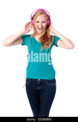 Trendy attractive young woman singing along to her music standing listening to her headphones , isolated on white Stock Photo