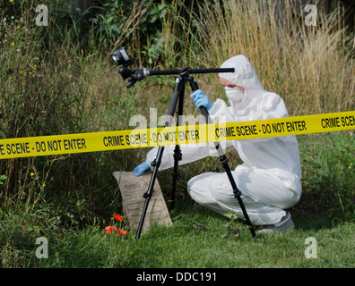 Forensic scientist checking for evidence behind a crime scene barrier Stock Photo