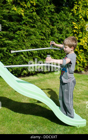 eight year old boy with crutches thinking about being adventurous on a garden slide. Stock Photo