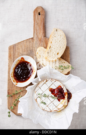 Baked Camembert cheese with thyme and toasted bread on wooden board Stock Photo