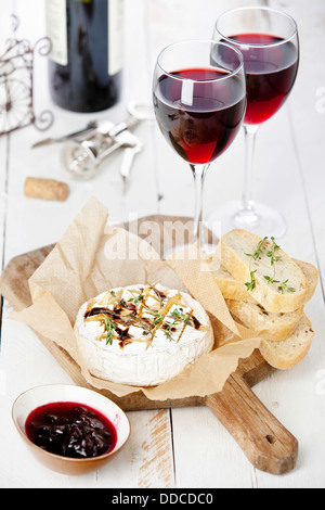 Baked Camembert cheese with red wine and toasted bread on wooden board Stock Photo