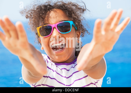 Beautiful, happy mixed race African American female girl child wearing sunglasses in vacation sunshine by blue tropical sea Stock Photo