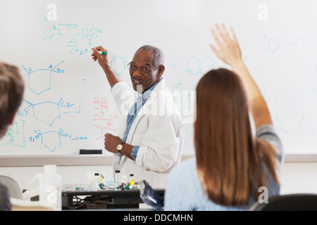 Student raising her hand in an engineering class while professor is at the white board writing about chemical bonds Stock Photo