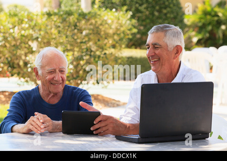 Senior man smiling showing a digital tablet to his father Stock Photo