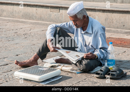Man offering scales for weighing awaits customers near the Haji Ali Mosque, Mumbai, India Stock Photo