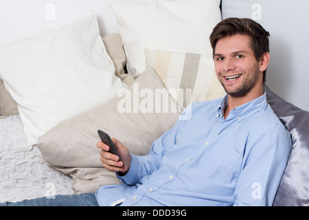 Young brunette man in blue shirt using cellphone on couch Stock Photo