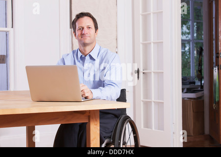 Man with spinal cord injury sitting in a wheelchair working on laptop Stock Photo