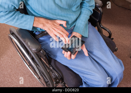Man with Friedreich's Ataxia in wheelchair using a smartphone with deformed hands Stock Photo