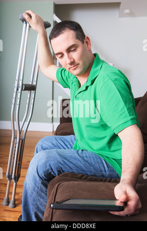 Man after anterior cruciate ligament (ACL) surgery with cane and an digital tablet at home Stock Photo