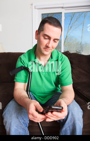 Man after anterior cruciate ligament (ACL) surgery with cane and a smartphone Stock Photo