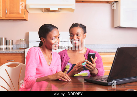 Two sisters working with smartphone and laptop at home, one with learning disability Stock Photo
