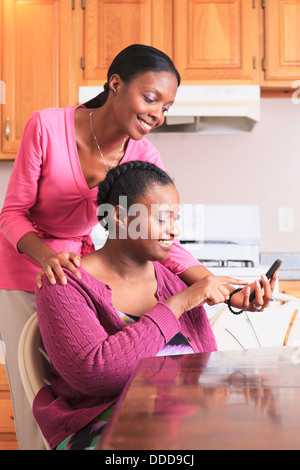 Two sisters looking at a smartphone in the kitchen, one with learning disability Stock Photo