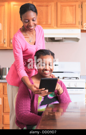 Two sisters looking at a digital tablet in the kitchen, one with learning disability Stock Photo