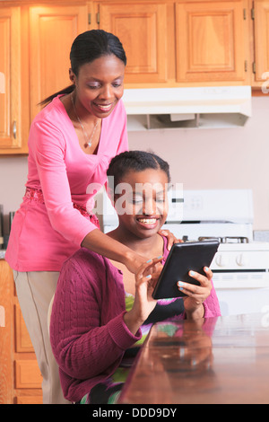 Two sisters looking at a digital tablet in the kitchen, one with learning disability Stock Photo