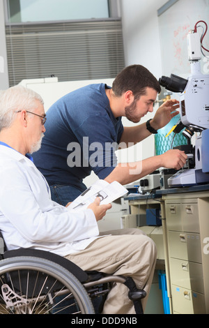 Professor with muscular dystrophy working with engineering student adjusting x-ray fluorescence analyzer in a laboratory Stock Photo