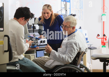 Professor muscular dystrophy working engineering students setting up adjustable stage chemical analysis instrument in laboratory Stock Photo