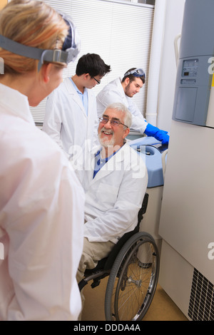 Professor with muscular dystrophy discussing bacteria culturing system with engineering students in a laboratory Stock Photo