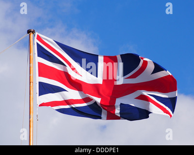 A Union Flag flying at the top of a flagpole against a partly cloudy blue sky Stock Photo