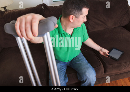 Man after anterior cruciate ligament (ACL) surgery with crutches and an digital tablet at home Stock Photo