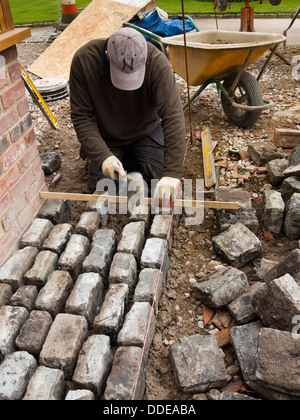self building house, hard landscaping, workman laying reclaimed granite setts around new build home Stock Photo