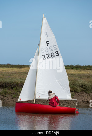 A small dinghy sails out of the harbour at Blakeney Stock Photo