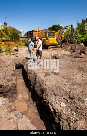 self building house, preparing site, workers inspecting trench dug for foundations by volvo digger Stock Photo