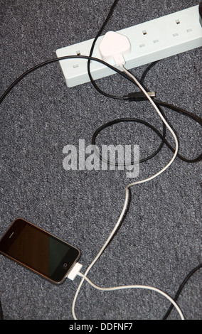 iPhone charging plugged into extension socket on floor Stock Photo