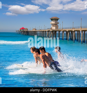 Teenager surfers surfing running jumping on surfboards at Huntington beach pier California Stock Photo