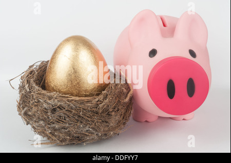 A golden egg in the bird nest with a piggy bank next to them Stock Photo