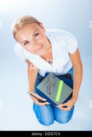Pretty school girl sitting on chair and looking up, isolated on blue background, high school, enjoying study, back to school Stock Photo