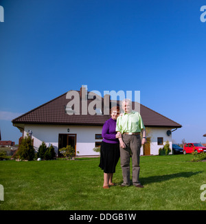 Senior smiling couple in the garden in front of their new house Stock Photo