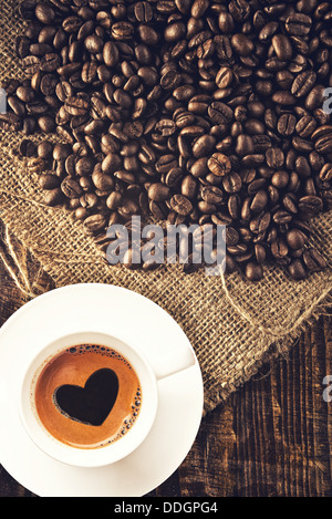 Coffee beans and coffee cup with heart shaped foam on jute canvas texture. Stock Photo