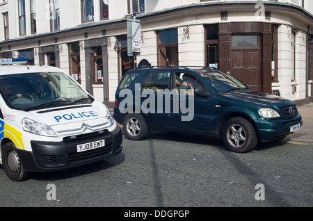 Police van drives past illegally parked 4X4 on double yellow lines Stock Photo