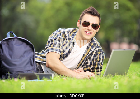 Smiling male student lying on a green grass and working on a laptop Stock Photo
