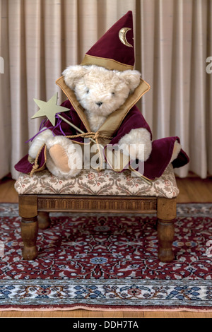 Creamy white stuffed teddy bear wearing burgundy and gold trimmed magician's coat and pointed hat holding a gold star magic wand Stock Photo