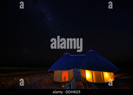 Illuminated chalet or cabin of the Sossus Dune Lodge at night, under a starry sky with the Milky Way Stock Photo
