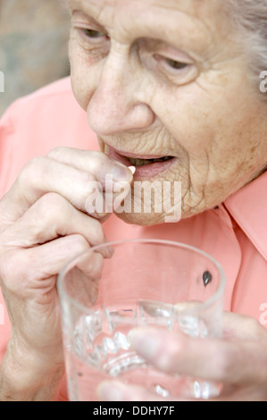 Elderly woman taking a Simvastatin tablet (statins) drugs that reduces the amount of cholesterol & triglycerides in the body Stock Photo