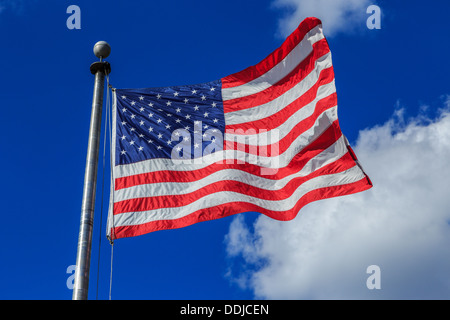 A photograph of an American flag blowing in the breeze against a very blue sky with some contrasting clouds Stock Photo